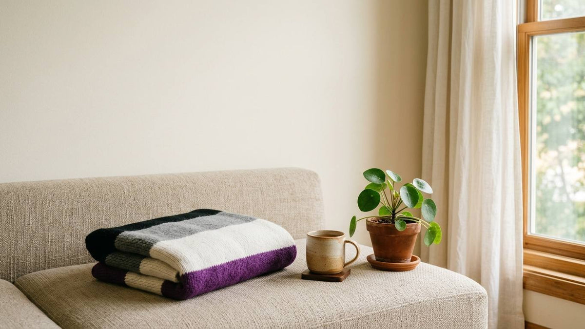 Black gray white and purple striped blanket folded on a cream couch beside a mug and plant