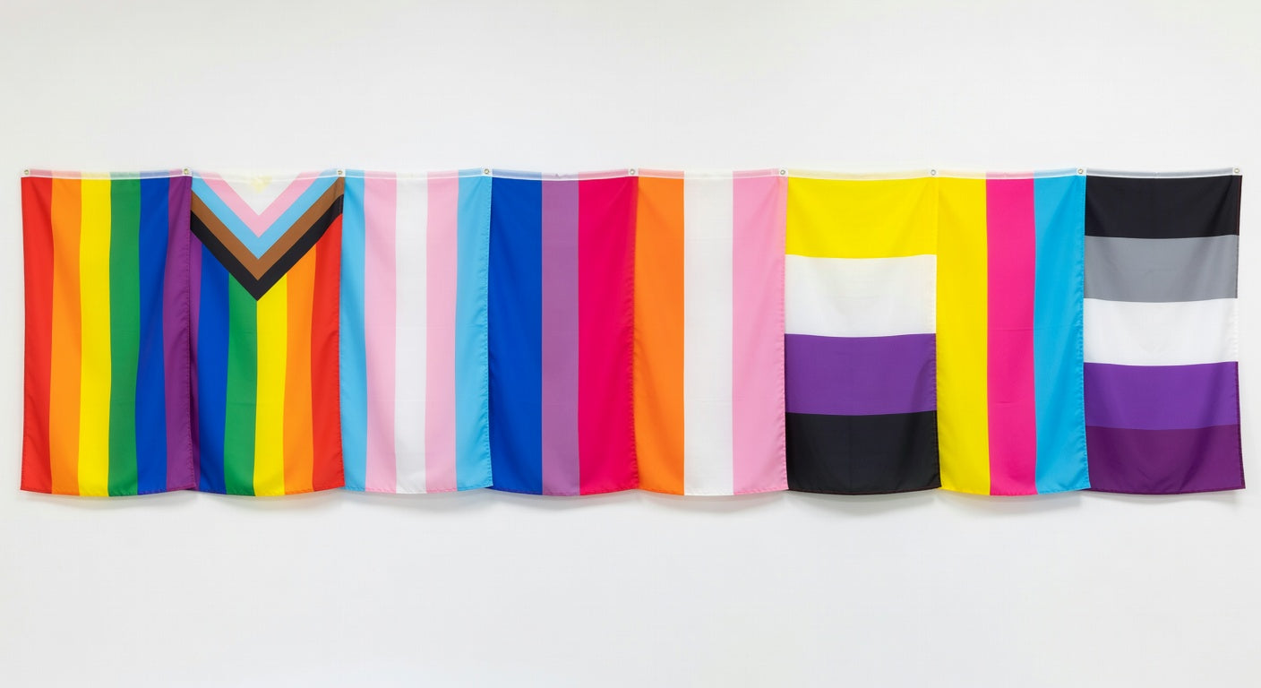 Row of different pride flags displayed on a wall including rainbow, progress, transgender, bisexual, non-binary, and pansexual flags