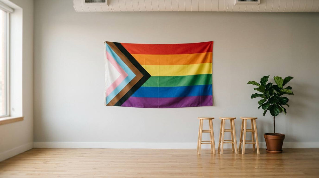Inclusive Progress Pride flag on a plain wall with stools and a plant in an empty event room