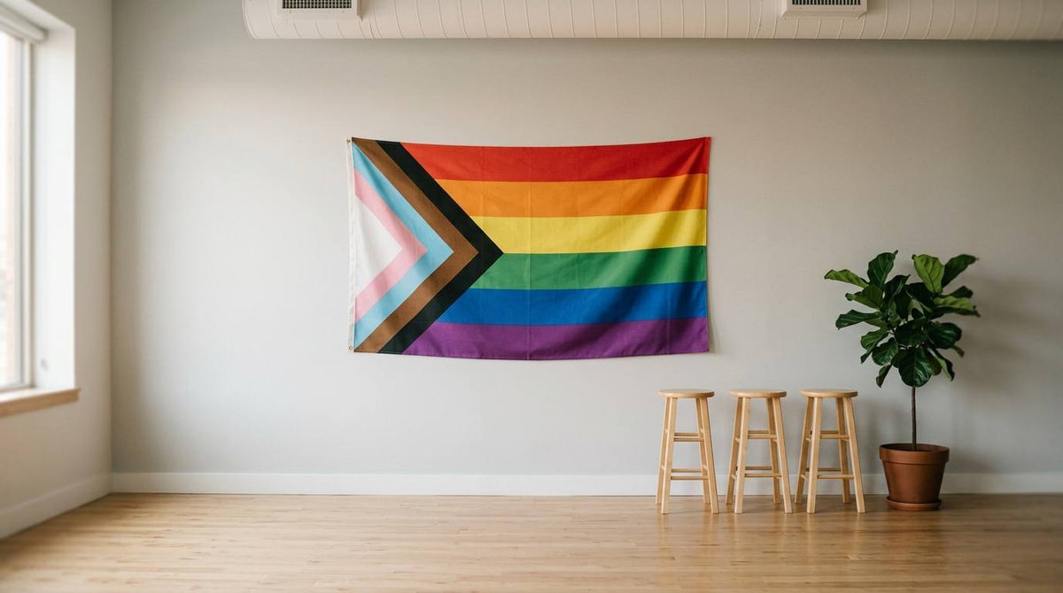 Inclusive Progress Pride flag on a plain wall with stools and a plant in an empty event room