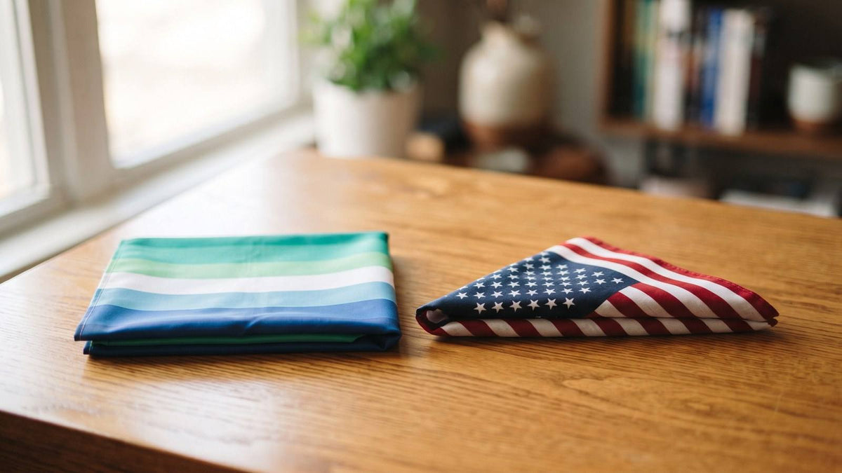 Folded gay men's pride flag beside a folded American flag on a sunlit wood table