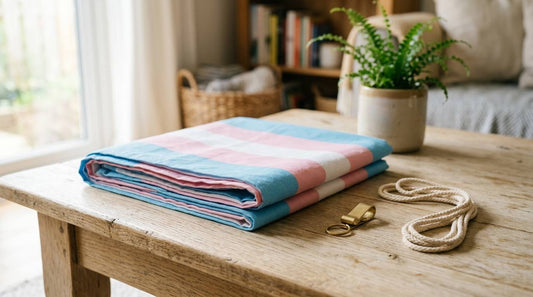 Folded transgender Pride flag on a wood table with a brass clip and hanging cord