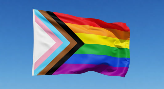 Progress Pride flag waving in the breeze against a blue sky